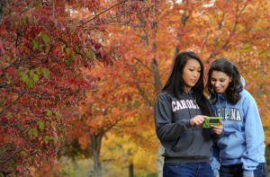 Image of students using their phones on campus with fall foliage in the background